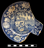 Pearlware saucer underglaze printed in medium blue in Milkmaid pattern. Continuous repeating floral border. One of two matching vessels from this assemblage. This piece is unmarked, but identical pattern and border have been found with the mark of Thomas Rathbone & Co., 1810 – 1845, Portobello, Scotland. 5.00” rim diameter, 1.00” vessel height.